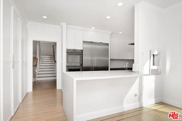 kitchen with white cabinets, crown molding, light wood-type flooring, kitchen peninsula, and stainless steel appliances