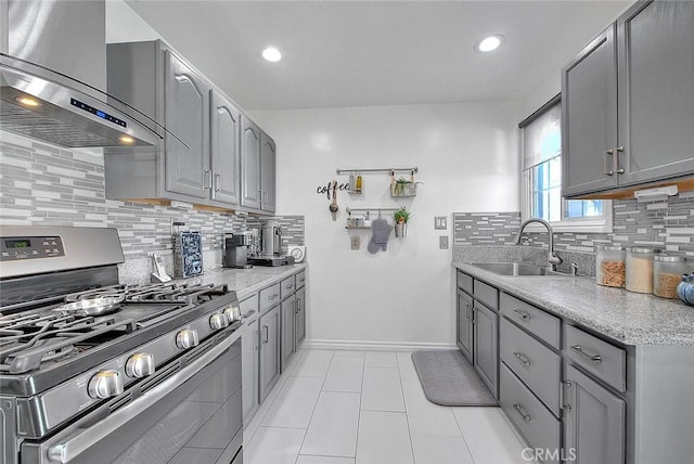 kitchen featuring gas range, sink, wall chimney exhaust hood, backsplash, and gray cabinets