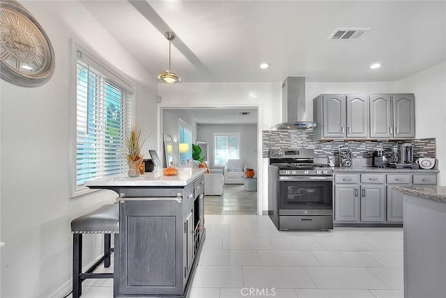 kitchen featuring gray cabinetry, wall chimney range hood, tasteful backsplash, pendant lighting, and stainless steel stove