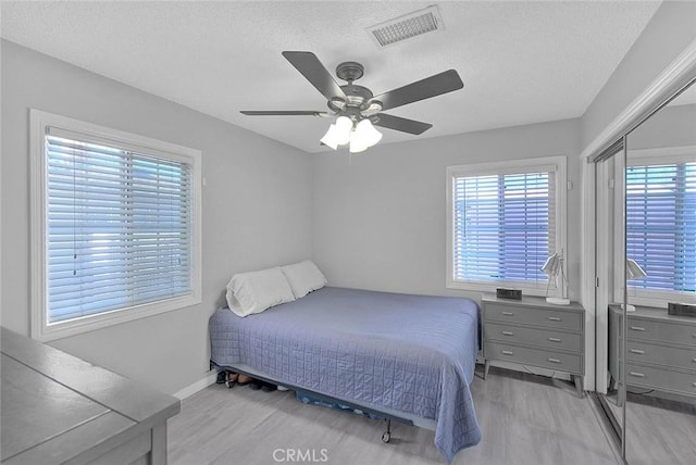 bedroom featuring ceiling fan, light hardwood / wood-style floors, and a textured ceiling