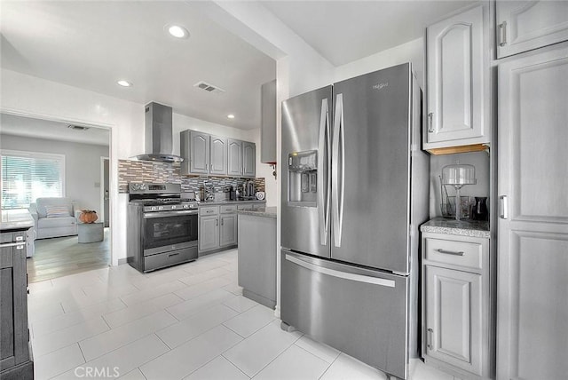 kitchen with gray cabinets, decorative backsplash, wall chimney exhaust hood, and appliances with stainless steel finishes