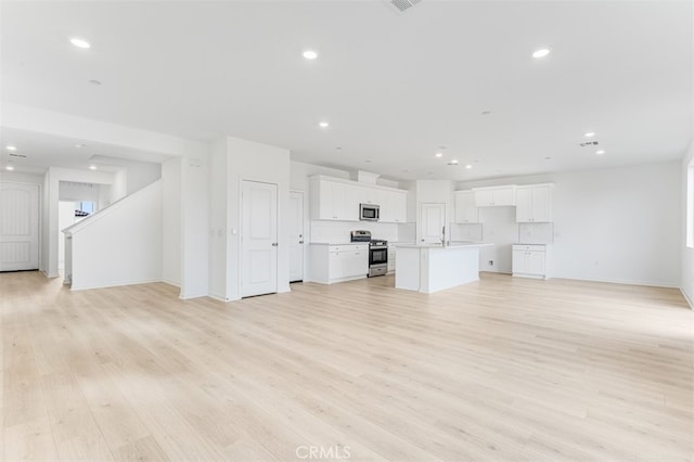 unfurnished living room with baseboards, recessed lighting, a sink, and light wood-style floors