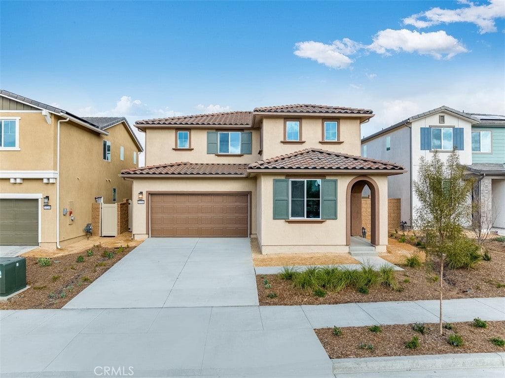 mediterranean / spanish-style home featuring driveway, an attached garage, a tile roof, and stucco siding