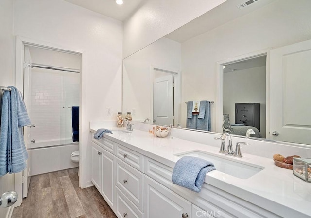 full bathroom featuring shower / bath combination with glass door, vanity, wood-type flooring, and toilet