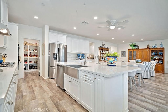 kitchen featuring a center island with sink, light hardwood / wood-style floors, white cabinetry, and appliances with stainless steel finishes