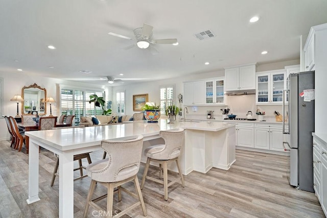 kitchen featuring stainless steel refrigerator, white cabinetry, gas stovetop, light hardwood / wood-style flooring, and an island with sink