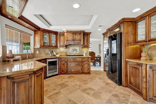 kitchen featuring a raised ceiling, sink, wine cooler, tasteful backsplash, and light stone counters