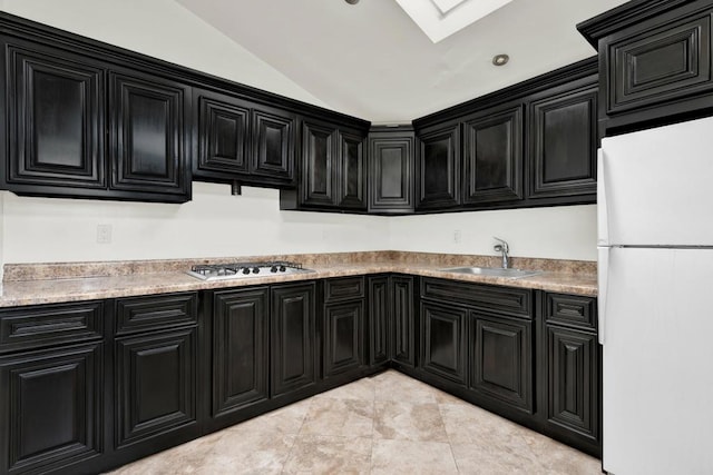 kitchen featuring lofted ceiling with skylight, sink, light tile patterned floors, white fridge, and stainless steel gas stovetop