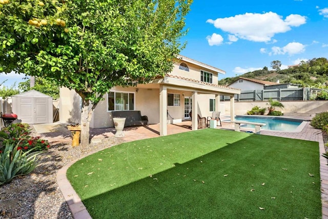 back of property with a yard, a fenced in pool, a storage unit, and a patio area