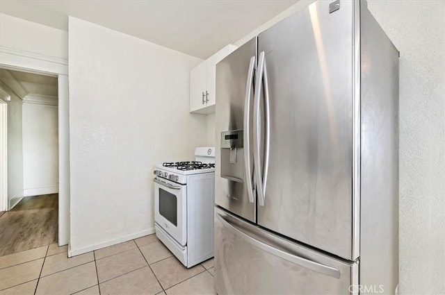 kitchen featuring white cabinets, stainless steel fridge, light tile patterned floors, and gas range gas stove