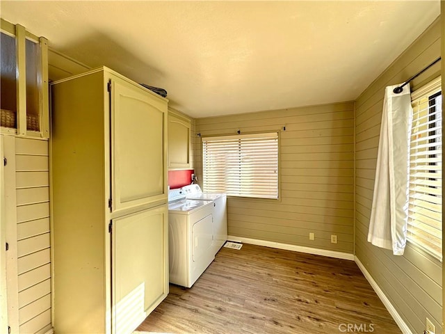 washroom with washer and dryer, cabinet space, wood walls, light wood finished floors, and baseboards