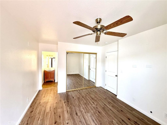 unfurnished bedroom featuring a closet, baseboards, wood finished floors, and a ceiling fan