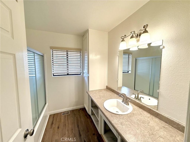 bathroom with vanity, wood finished floors, visible vents, baseboards, and enclosed tub / shower combo