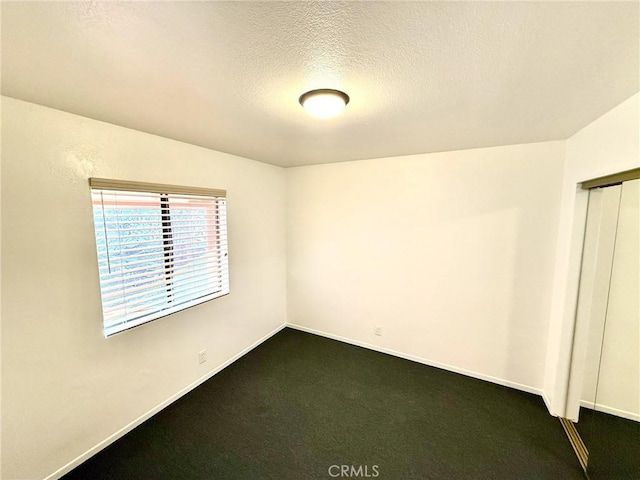 spare room featuring a textured ceiling, baseboards, and dark colored carpet