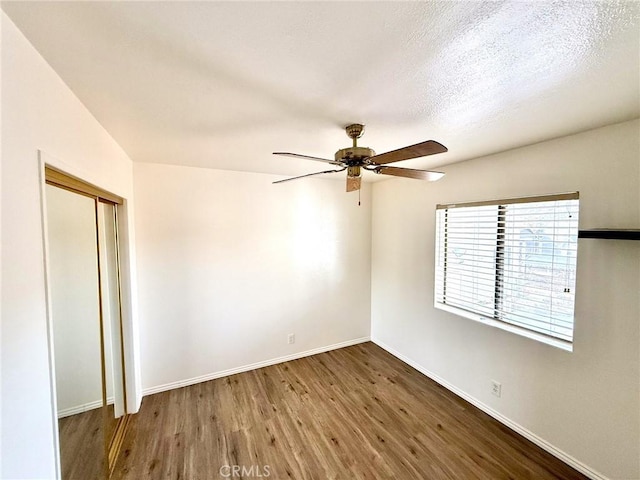 spare room with baseboards, a textured ceiling, wood finished floors, and a ceiling fan