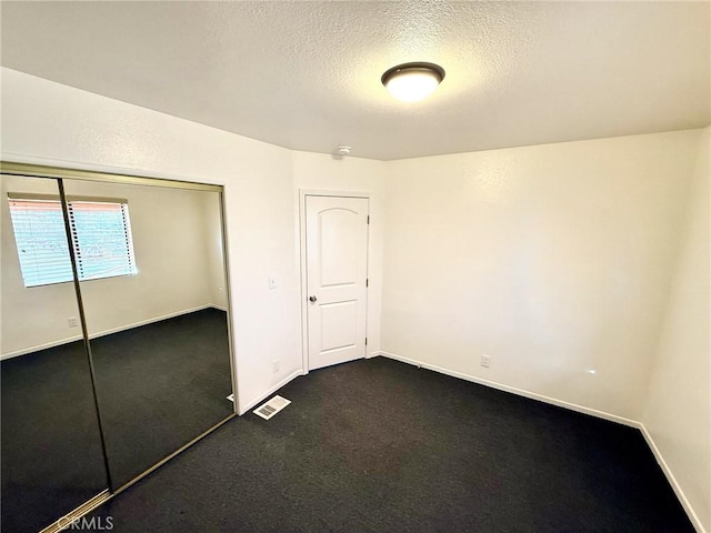 unfurnished bedroom featuring visible vents, a textured ceiling, dark carpet, a closet, and baseboards