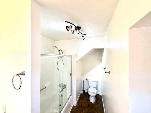 bathroom featuring baseboards, toilet, and shower / bath combination with glass door