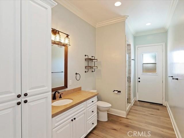 bathroom featuring a shower with shower door, hardwood / wood-style flooring, ornamental molding, vanity, and toilet