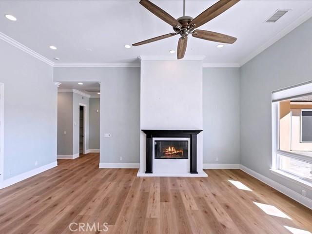 unfurnished living room featuring a multi sided fireplace, ornamental molding, ceiling fan, and light wood-type flooring