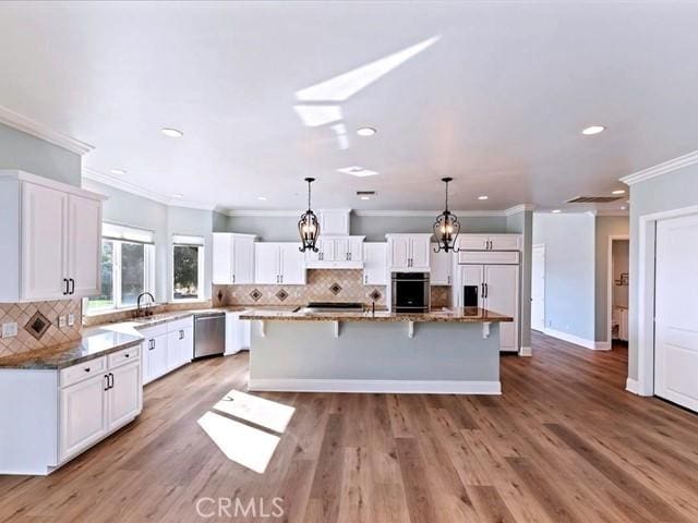 kitchen with decorative light fixtures, dark stone countertops, white cabinets, a center island, and stainless steel appliances