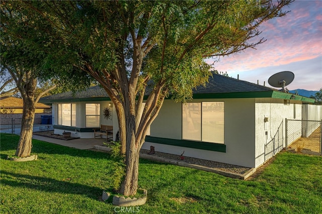 back house at dusk featuring a patio area and a yard