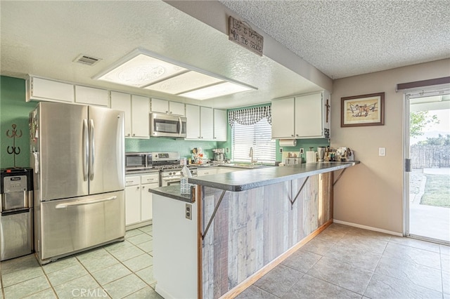 kitchen featuring kitchen peninsula, appliances with stainless steel finishes, white cabinetry, and plenty of natural light