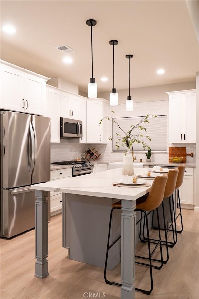 kitchen with appliances with stainless steel finishes, light wood-type flooring, decorative light fixtures, a center island, and white cabinetry