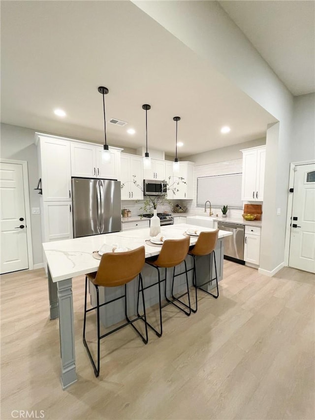 kitchen with light stone counters, stainless steel appliances, decorative light fixtures, white cabinets, and a center island