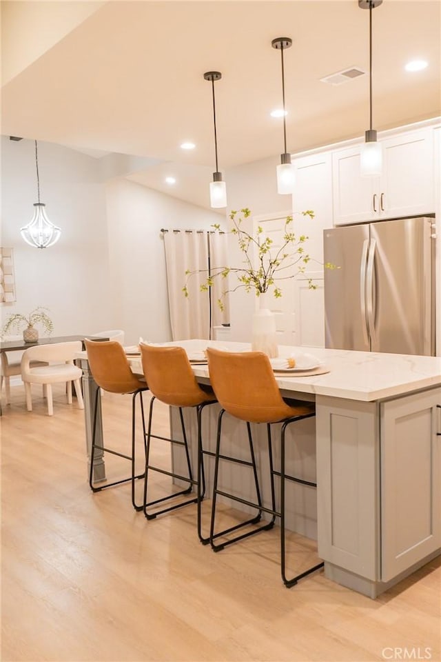 interior space featuring stainless steel fridge, white cabinetry, and hanging light fixtures