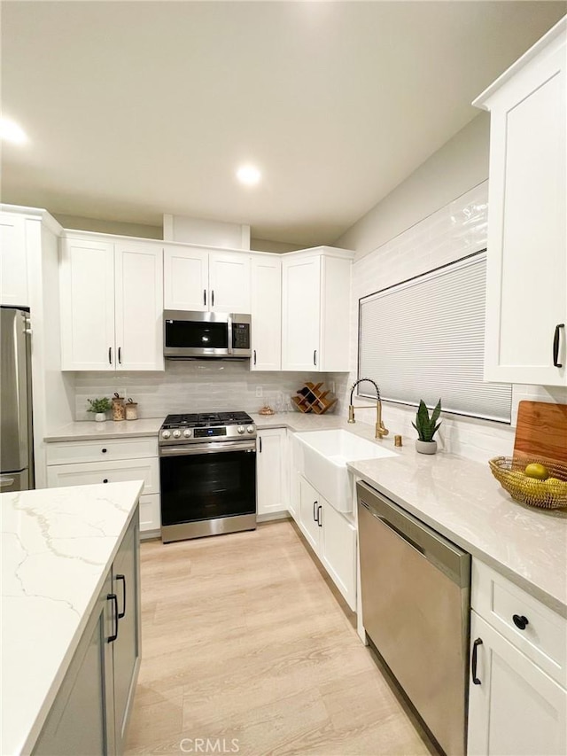 kitchen with white cabinets, stainless steel appliances, light stone counters, and sink