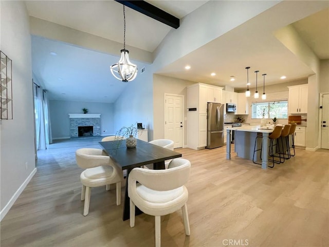 dining area with lofted ceiling with beams, light hardwood / wood-style floors, a stone fireplace, and an inviting chandelier