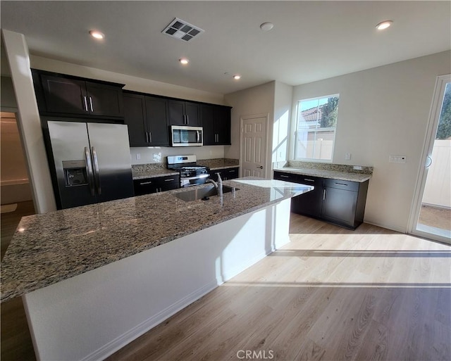 kitchen with sink, a center island with sink, stainless steel appliances, and light hardwood / wood-style floors