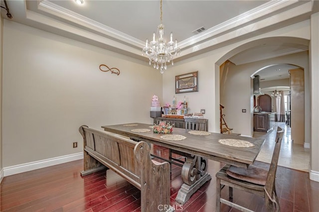 dining space featuring dark hardwood / wood-style floors, an inviting chandelier, a tray ceiling, and ornamental molding