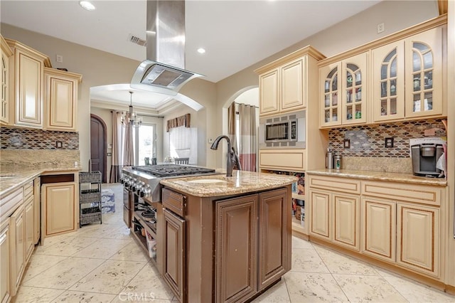 kitchen with stainless steel microwave, a kitchen island with sink, ornamental molding, island exhaust hood, and a chandelier