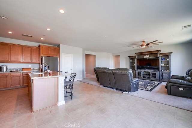 kitchen with light stone countertops, sink, stainless steel refrigerator with ice dispenser, an island with sink, and a breakfast bar area