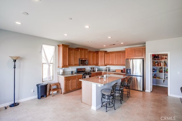 kitchen with a kitchen bar, appliances with stainless steel finishes, light stone countertops, sink, and an island with sink