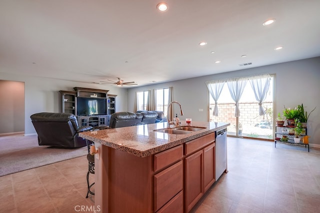 kitchen featuring ceiling fan, dishwasher, sink, light stone counters, and a kitchen island with sink