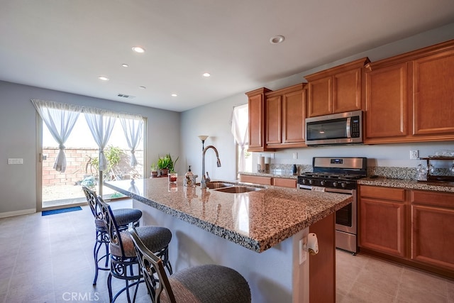 kitchen with a kitchen bar, a kitchen island with sink, sink, appliances with stainless steel finishes, and light stone counters