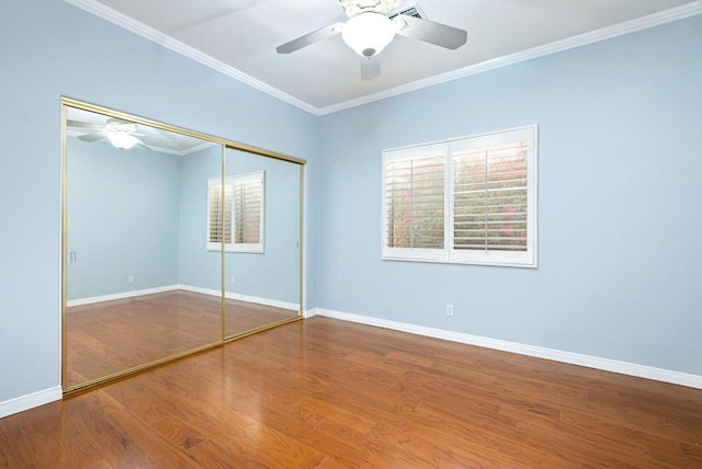 unfurnished bedroom featuring ceiling fan, wood-type flooring, ornamental molding, and a closet