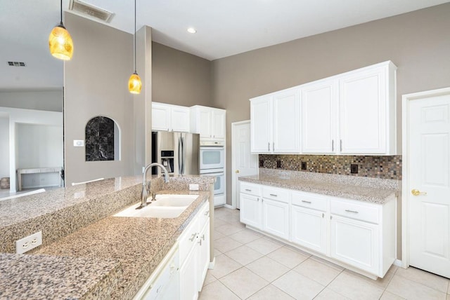 kitchen featuring white cabinets, stainless steel fridge, sink, and hanging light fixtures