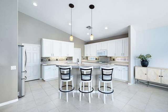 kitchen featuring tasteful backsplash, a center island with sink, white cabinetry, and hanging light fixtures