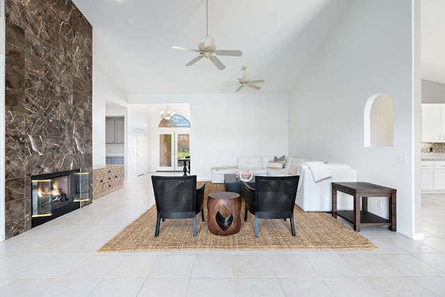 tiled living room with ceiling fan with notable chandelier, high vaulted ceiling, tile walls, and a tiled fireplace