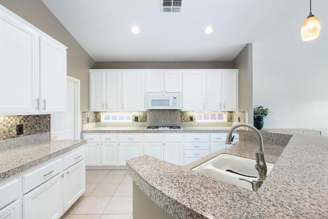 kitchen with pendant lighting, backsplash, sink, light tile patterned floors, and white cabinetry