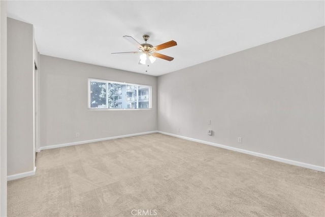 unfurnished room with a ceiling fan, light carpet, and baseboards