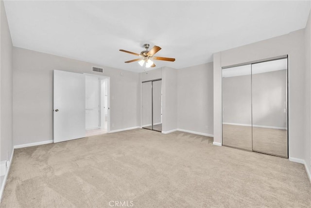 unfurnished bedroom featuring light carpet, baseboards, visible vents, ceiling fan, and multiple closets