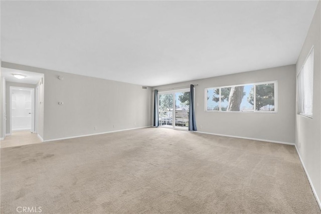 spare room featuring light carpet and baseboards