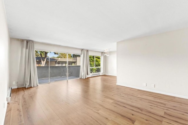 unfurnished room featuring baseboard heating, a notable chandelier, and light hardwood / wood-style floors