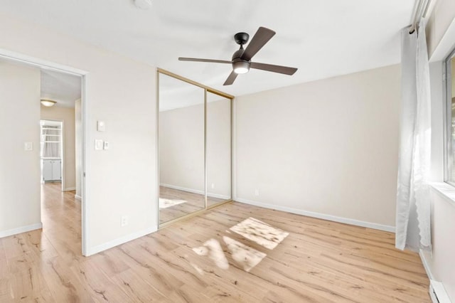 unfurnished bedroom featuring baseboard heating, ceiling fan, light hardwood / wood-style flooring, and a closet