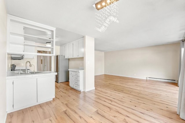 kitchen featuring stainless steel fridge, baseboard heating, light wood-type flooring, white cabinets, and sink