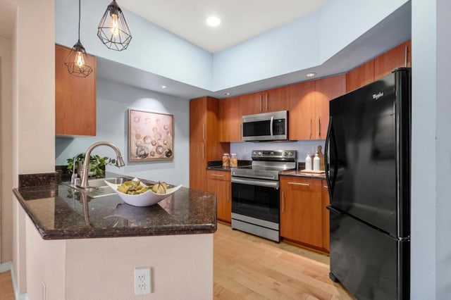 kitchen with decorative light fixtures, sink, kitchen peninsula, stainless steel appliances, and light hardwood / wood-style flooring